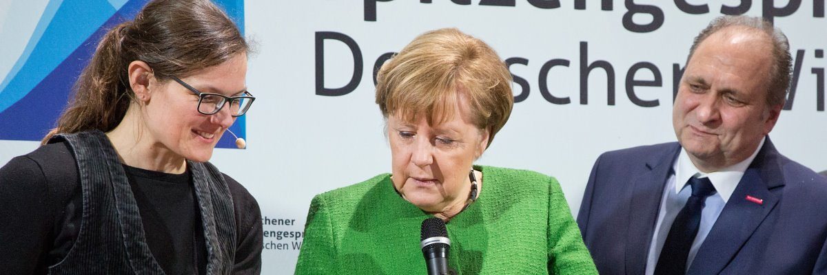 Bundeskanzlerin Angela Merkel (M.) besucht gerne das Handwerk der IHM. Zwei Frau und ein Mann stehen zusammen und betrachten etwas außerhalb des Bildes. Die Frau in der Mitte hält ein Mikrofon.