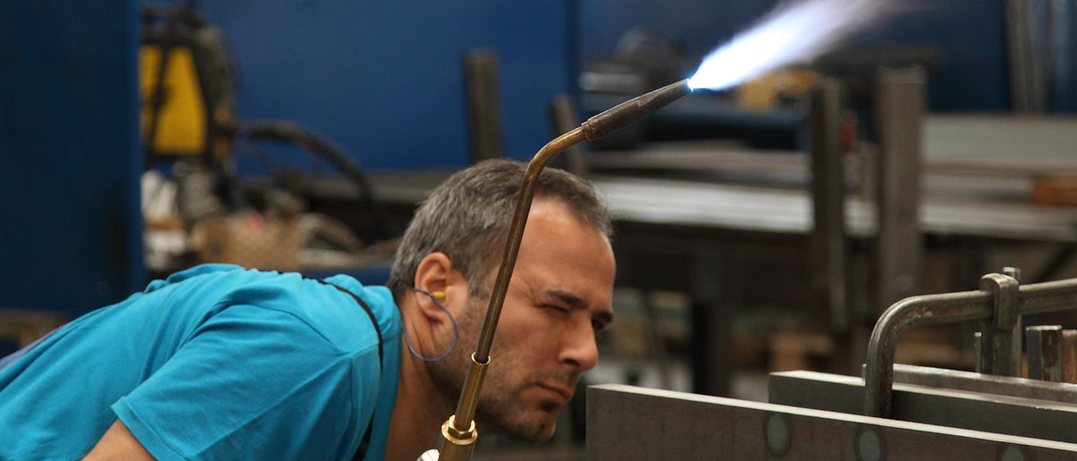 Ein Mann hält ein Schweßgerät in der Hand und schaut auf eine Metallplatte.