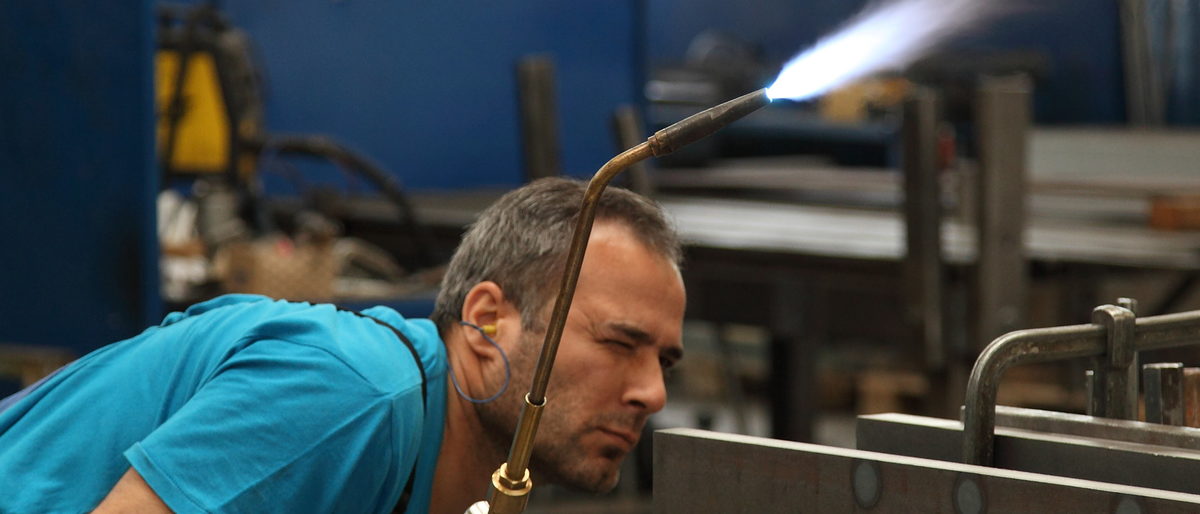 Metallbauer können im Bildungs- und Technologiezentrum einen Meister-Vorbereitungskurs belegen. Ein Mann hält ein Schweßgerät in der Hand und schaut auf eine Metallplatte.