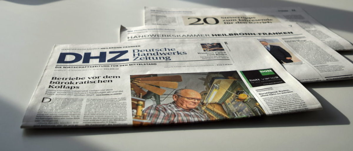 Die Deutsche Handwerks Zeitung informiert Betriebe zu aktuellen Themen Eine Zeitung liegt in der Häfte gefaltet auf einem weißen Tisch. Ihre einzelnen Bücher sind etwas auseinander geschoben.