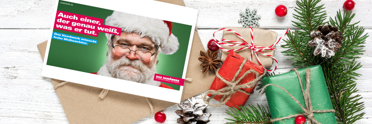 Zu Weihnachten gibt es spezielle Angebote der Imagekampagne. Weihnachtspostkarte, brauner Briefumschlag und weihnachtliche Dekoration liegen auf weißem Holz.