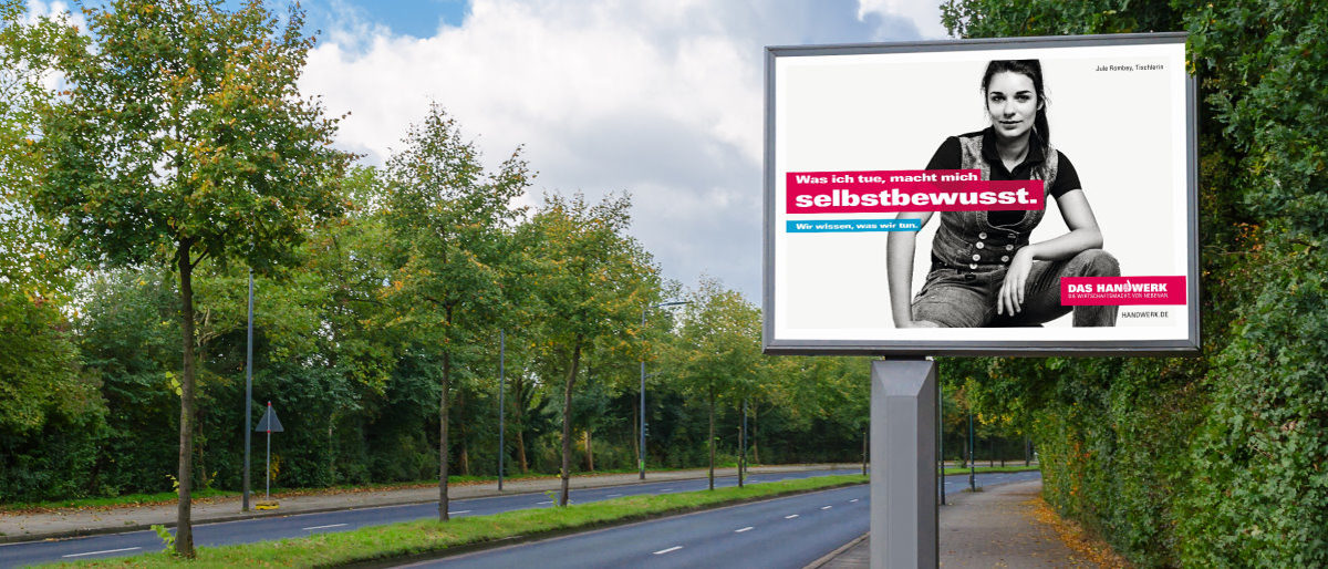 Die neuen Plakate der Imagekampagne sind auch in der Region zu sehen. Eine hohe Plakatwand steht an einer vierspurigen Straße mit Bäumen auf dem Mittelstreifen. Es sind keine Autos zu sehen.