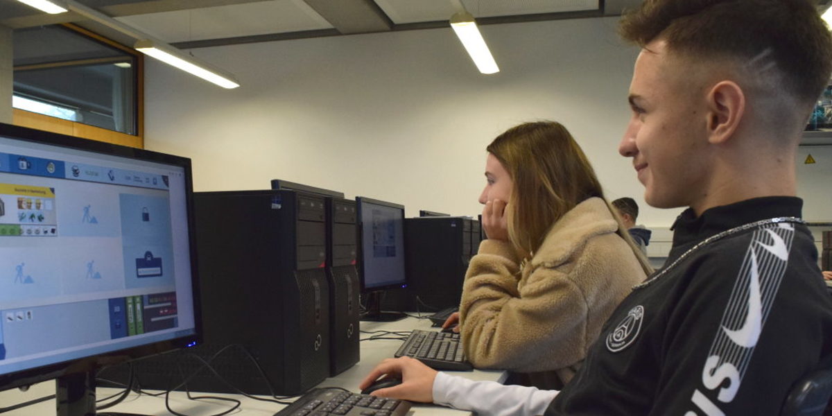 Schüler können am Wettbewerb des Online-Spiels Meisterpower teilnehmen Ein Junge und ein Mädchen sitzen konzentriert vor Computerbildschirmen in einen Klassenzimmer.