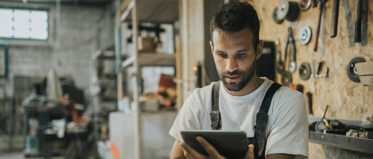 Web-Seminare für Handwerker - kostenfrei und wo Sie wollen. Handwerker in Werkstatt mit Tablet in der Hand, schaut Web-Seminar