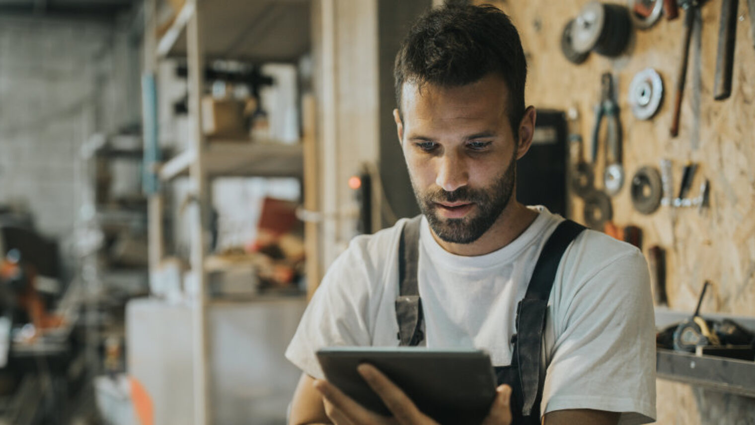 Handwerker in Werkstatt mit Tablet in der Hand, schaut Web-Seminar.