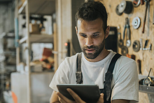 Handwerker in Werkstatt mit Tablet in der Hand, schaut Web-Seminar.