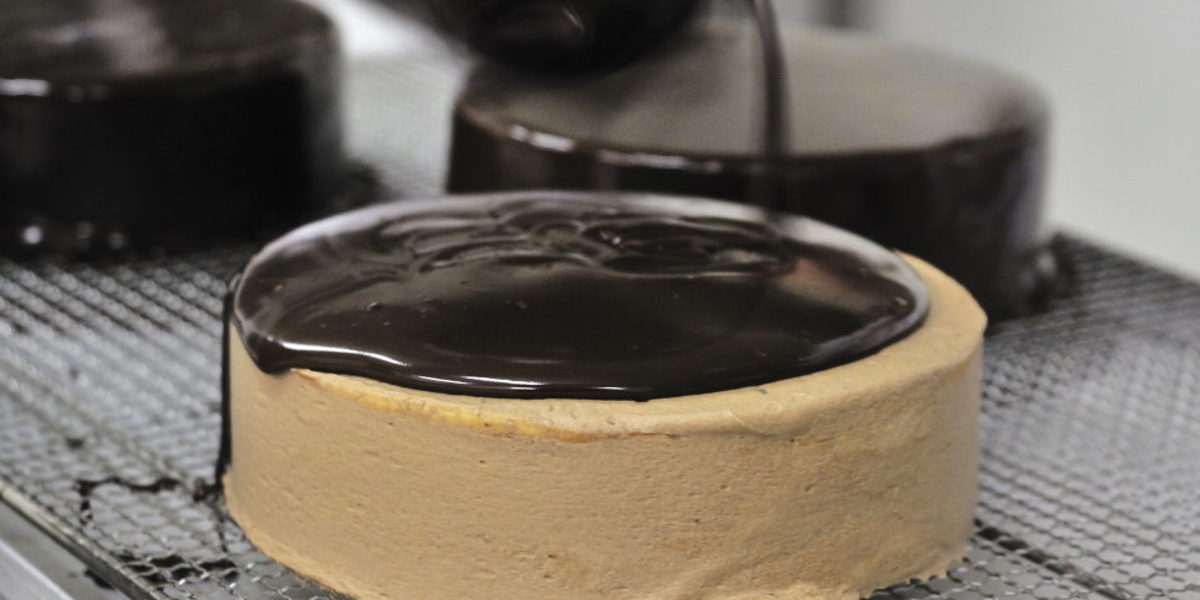 Im Vordergrund fließt Schokolade über eine Torte. Im Hintergrund sind zwei fertige Schokoladentorten zu sehen. 