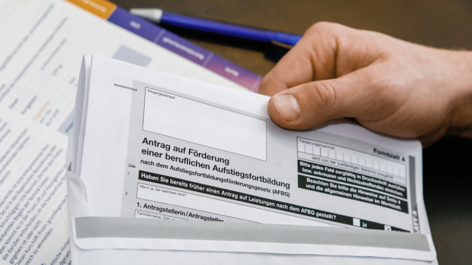 Eine Hand steckt auf einem Schreibtisch ein Antragsformular auf Ausbildungsförderung in einen Briefumschlag.