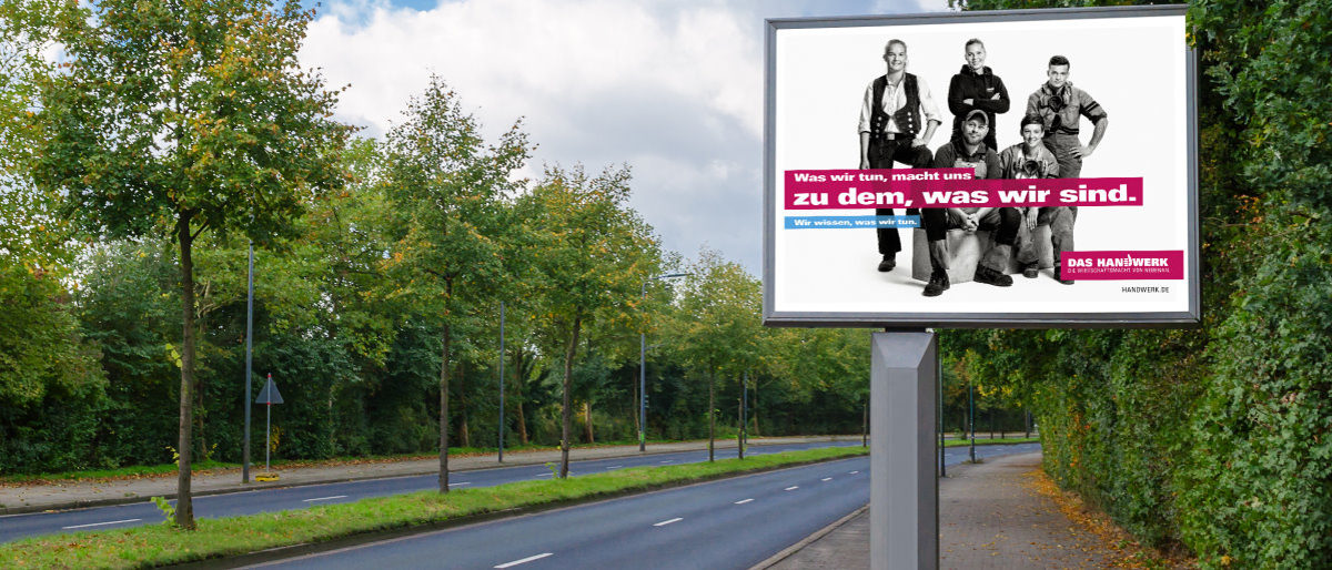 Neue Motive der Imagekampagne zeigen fünf stolze Handwerker. Ein Plakat zeigt fünf Handwerker. Es ist auf einer großen Werbetafel an einer vierspurigen Straße mit Bäumen in der Mitte.