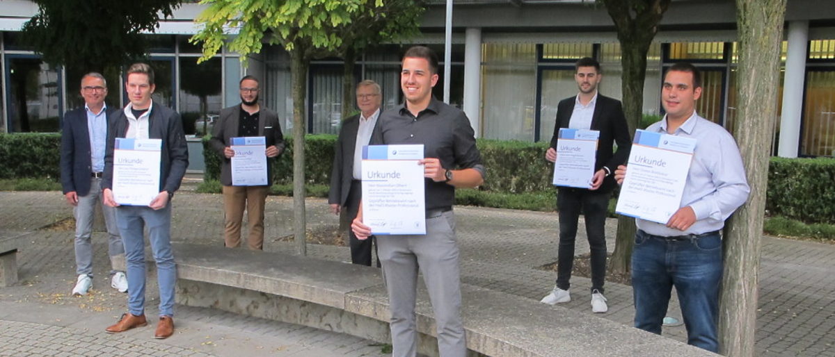 Die neuen Betriebswirte mit ihrer Prüfungskommission. Sieben Personen stehen vor dem BTZ. Fünf davon halten eine Urkunde in der Hand.