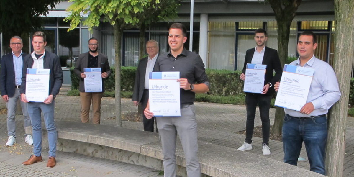 Die neuen Betriebswirte mit ihrer Prüfungskommission. Sieben Personen stehen vor dem BTZ. Fünf davon halten eine Urkunde in der Hand.