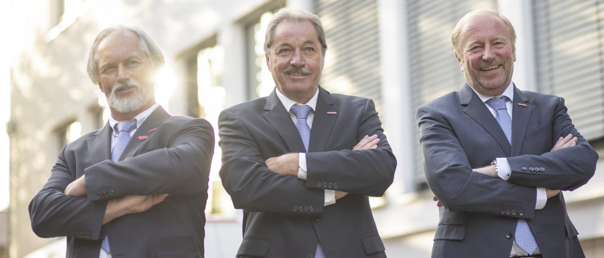 Präsidium (v.l.): Markus May, Kurt Georg Schreiber und Ulrich Bopp. Drei Männer in blauen Anzügen stehen mit verschränkten Armen vor einem Gebäude.