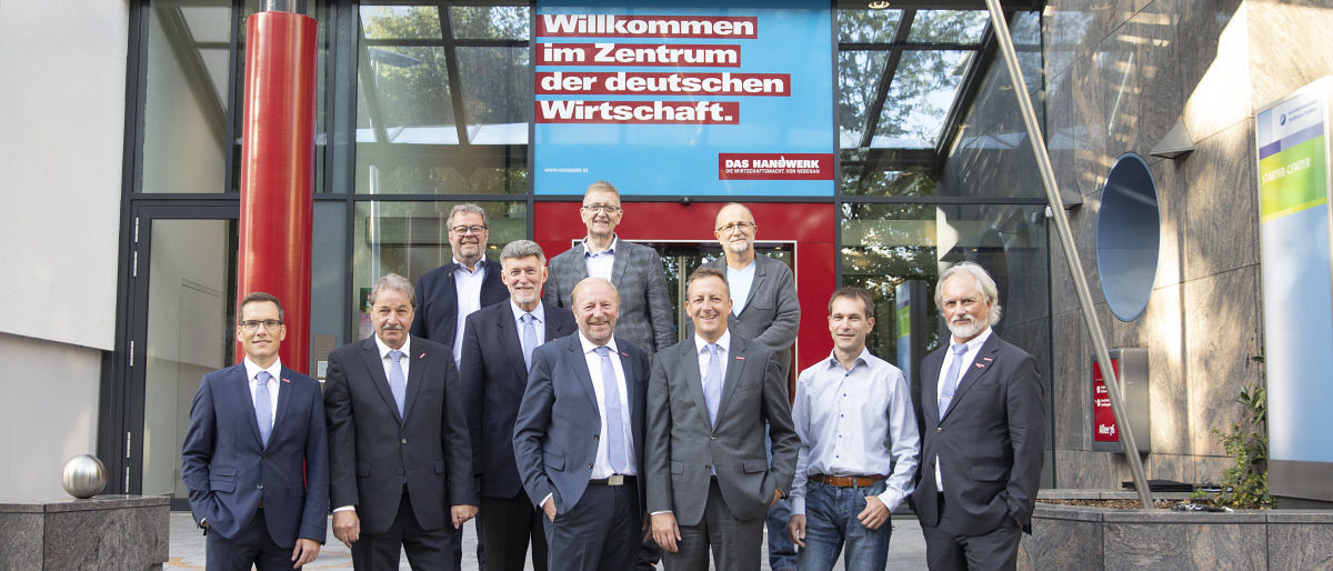 Der Vorstand der Handwerkskammer Heilbronn-Franken. Eine Gruppe von zehn Männern steht vor dem Eingang zu einem Gebäude und lächelt in die Kamera.