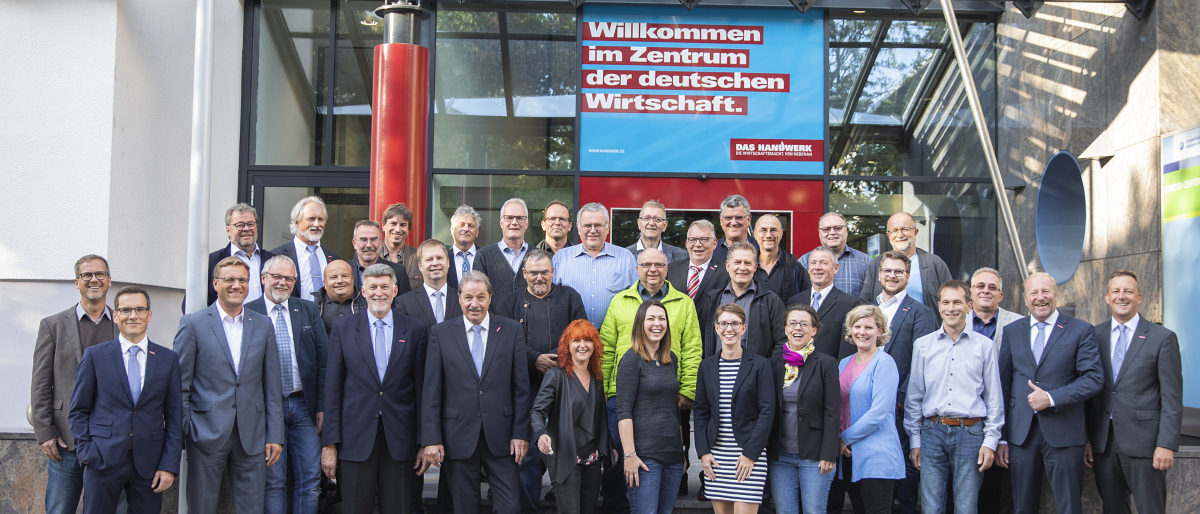 Die Vollversammlung der Handwerkskammer Heilbronn-Franken 2019-2014. Eine große Gruppe Menschen steht vor dem Eingang eines Gebäudes und lächelt in die Kamera.