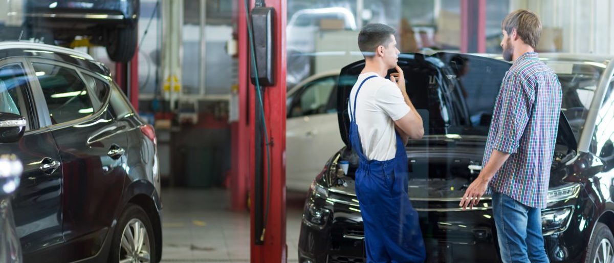 Schnell und unkompliziert Handwerker in der Nähe finden. Zwei Männer stehen in einer Kfz-Werkstatt und unterhalten sich.