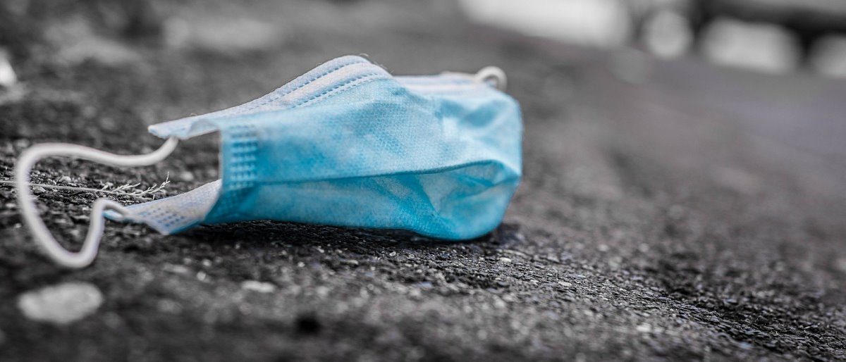 Der Lockdown in Deutschland ist bis Ende Januar verlängert worden. Eine einfache blaue Atemschutzmaske zum einmaligen Gebrauch liegt auf dem Asphalt einer Straße. Im Hintergrund ist ein Auto.