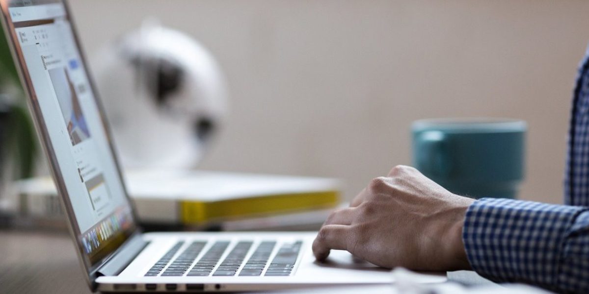Betriebe können ihre Lehrstellen für das Online-Speed-Dating eintragen Jemand sitzt an einem Tisch vor einem geöffneten Laptop, nur Hand auf dem Mousepad und Teil des Oberkörpers sind zu sehen.