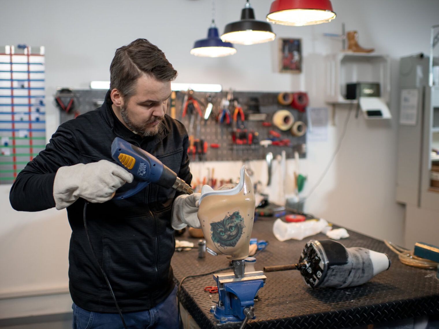 Ein Mann steht in einer Werkstatt und bearbeitet eine Prothese, auf der eine Katze abgebildet ist, mit einem Werkzeug.