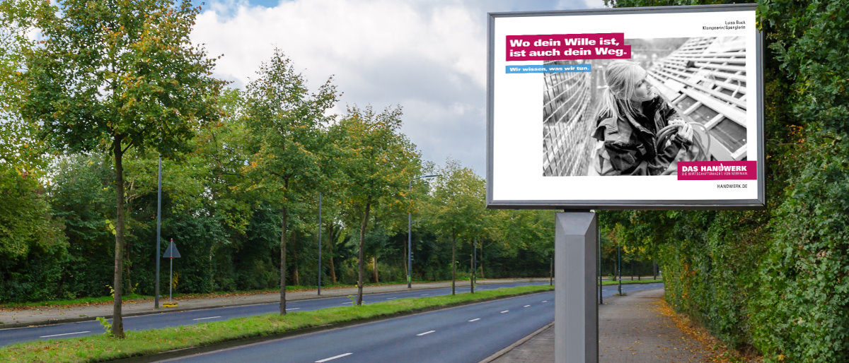 Neue Plakate der Imagekampagne werben deutschlandweit für das Handwerk Eine Plakatfläche an einer vierspurigen Straße mit Bäumen in der Mitte mit einem Werbeplakat des Handwerks auf einer Stele.