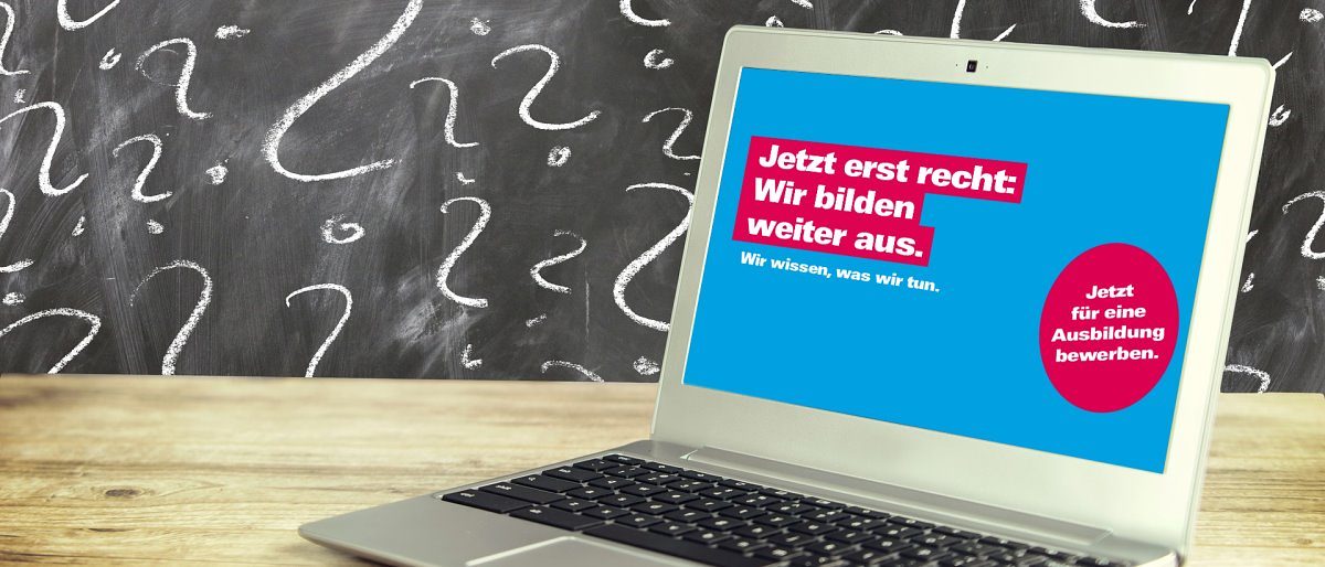 Tipps, wie Handwerksbetriebe Ausbildungsplätze trotz Corona besetzen. Ein geöffneter Laptop steht auf einer Holzplatte. Im Hintergrund eine Tafel mit Fragezeichen aus Kreide geschrieben.
