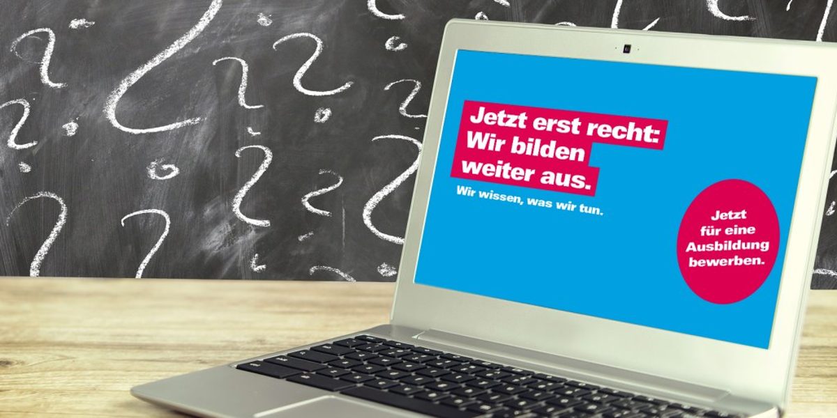 Tipps, wie Handwerksbetriebe Ausbildungsplätze trotz Corona besetzen. Ein geöffneter Laptop steht auf einer Holzplatte. Im Hintergrund eine Tafel mit Fragezeichen aus Kreide geschrieben.