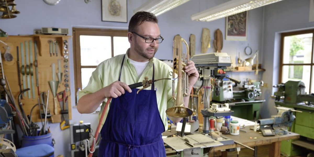 Handwerker steht in seiner Werkstatt und bearbeitet eine Trompete. 
