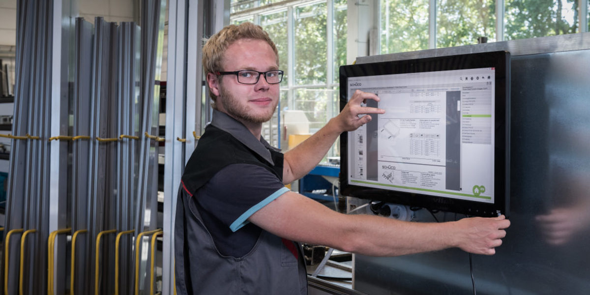 Innovationspreis BW - Aufmerksamkeit und Würdigung für Innovative Ideen Junger Handwerker in der Werkstatt arbeitet am Touch-Monitor und blickt in die Kamera.