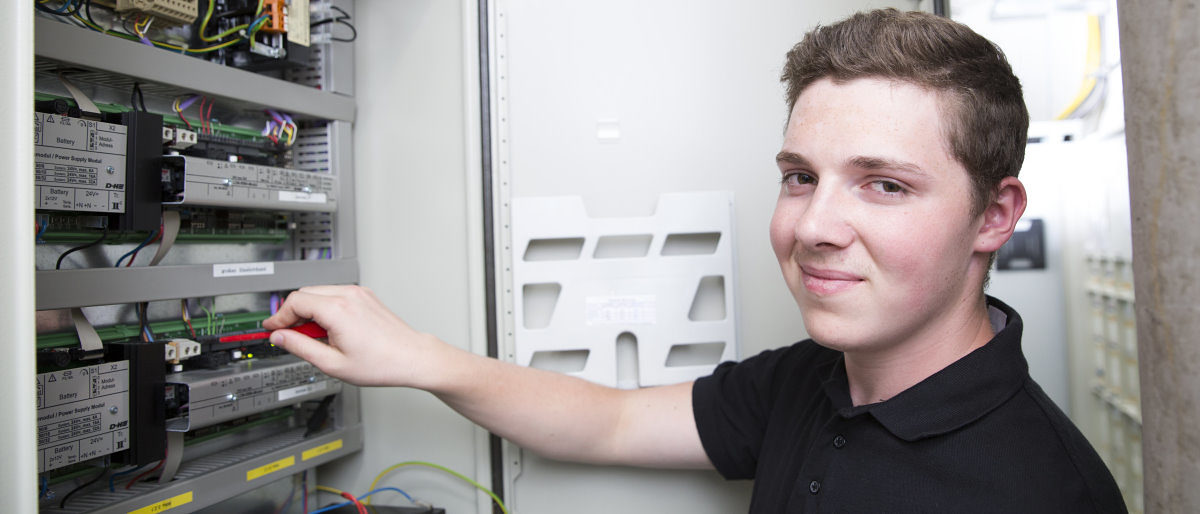 Kammern werben gemeinsam für freie Ausbildungsplätze. Junger Mann steht vor einem Schaltschrank, stellt mit einem Werkzeug etwas ein und hat sich lächelnd halb zur Kamera gedreht.