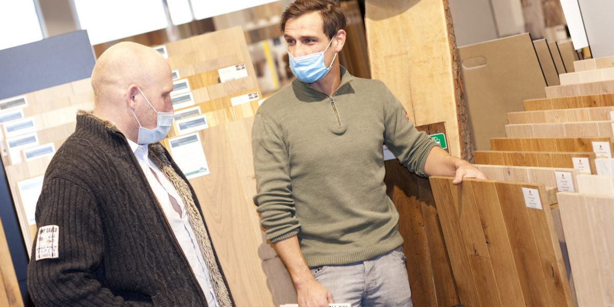 Die Stimmung im Handwerk hat sich laut aktueller Umfrage verbessert. Zwei Männer mit medizinischen Masken stehen in einem Raum mit vielen verschiedenen Ansichtsexemplaren von Parkettböden.