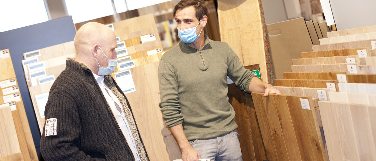 Die Stimmung im Handwerk hat sich laut aktueller Umfrage verbessert. Zwei Männer mit medizinischen Masken stehen in einem Raum mit vielen verschiedenen Ansichtsexemplaren von Parkettböden.
