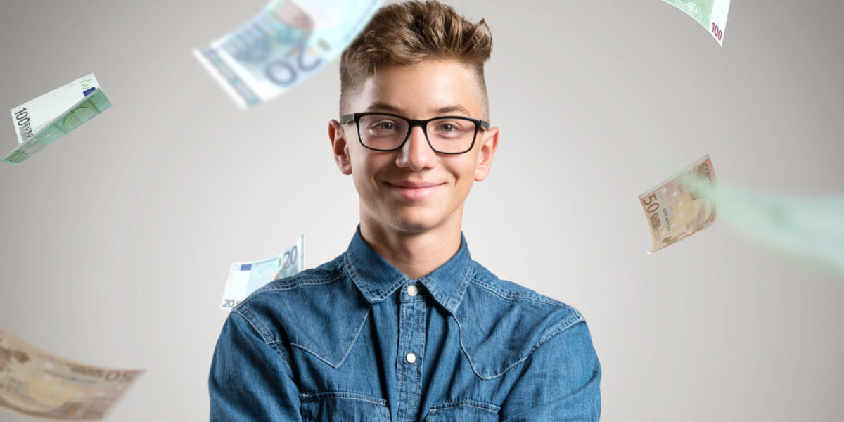 Porträt eines jungen Mannes mit Brille und in Jeanshemd vor einem grauen Hintergrund. Um ihn herum regnet es Euroscheine.