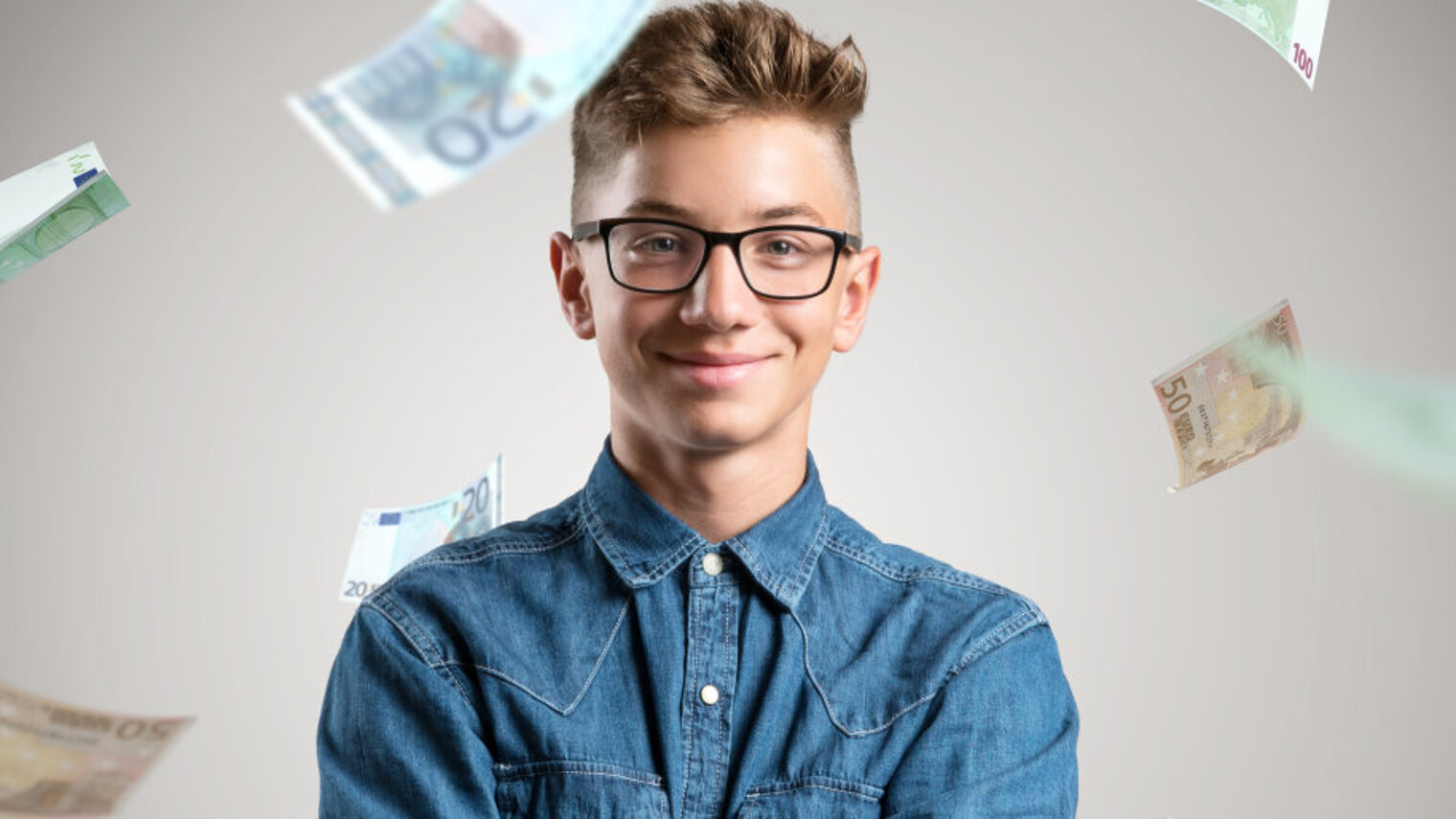 Porträt eines jungen Mannes mit Brille und in Jeanshemd vor einem grauen Hintergrund. Um ihn herum regnet es Euroscheine.