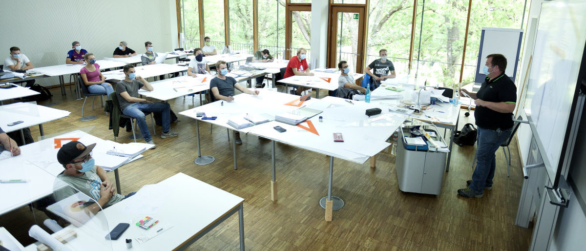 Ministerium legt Eckpunkte zum Unterricht an Berufsschulen fest. Blick in ein Klassenzimmer, Lehrer spricht vor Schülern an Tischen sitzend mit Abstand und Mund-Nasen-Schutz.