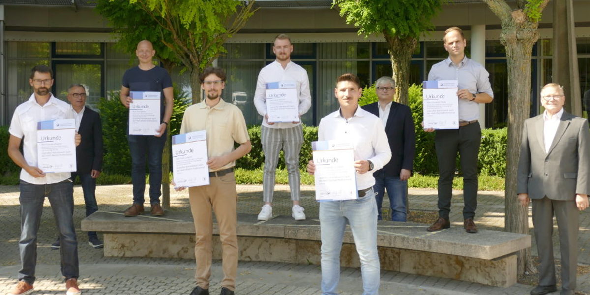 Sechs Betriebswirt-Absolventen mit ihrer Urkunde in der Hand stehen vor dem BTZ, dahinter die Prüfer.