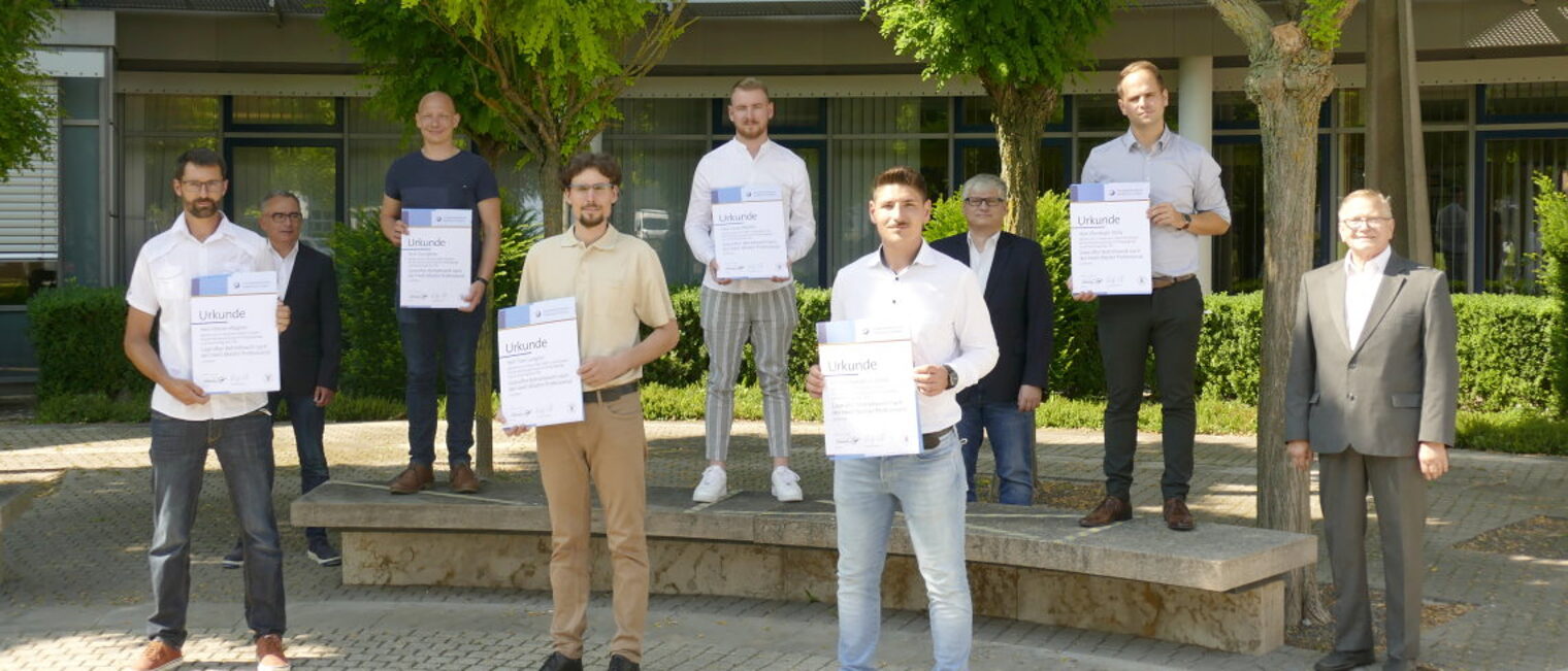 Sechs Betriebswirt-Absolventen mit ihrer Urkunde in der Hand stehen vor dem BTZ, dahinter die Prüfer.