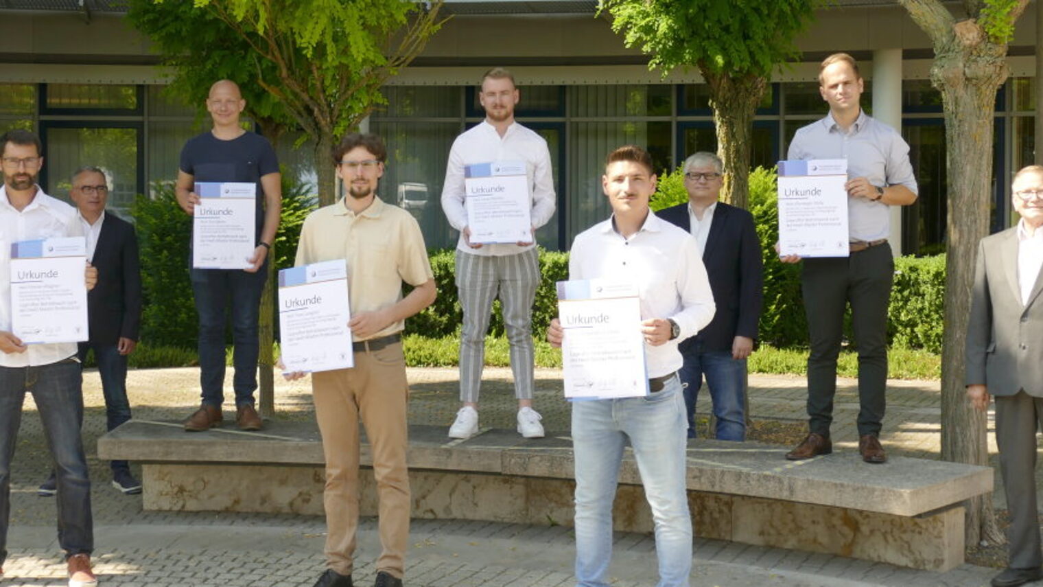 Sechs Betriebswirt-Absolventen mit ihrer Urkunde in der Hand stehen vor dem BTZ, dahinter die Prüfer.