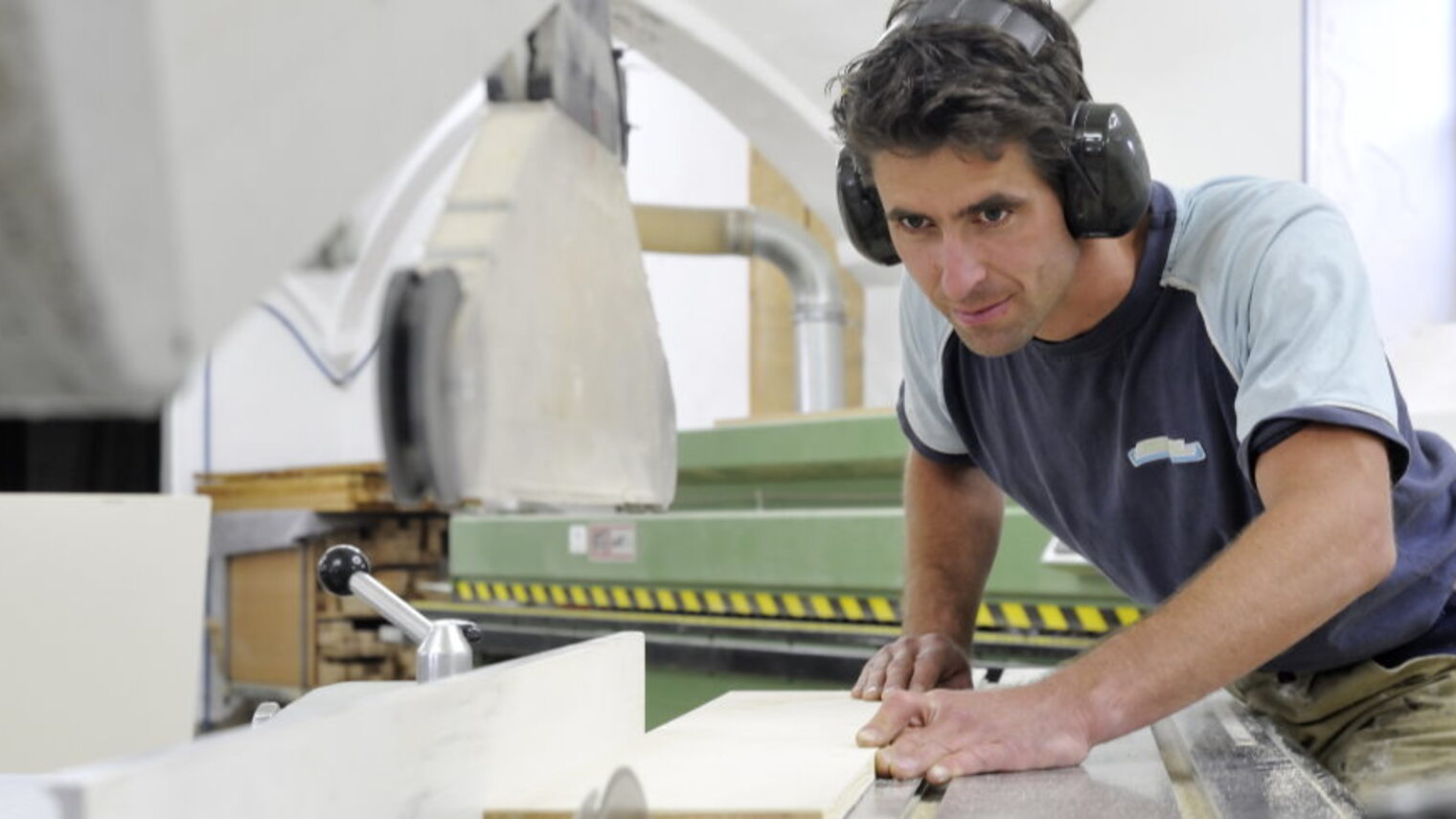 Schreiner bei der Arbeit in der Werkstatt, sägt Holzbrett an großer Maschine