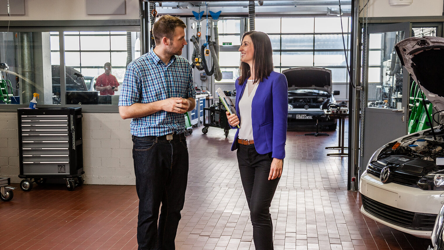 Ein Mann und eine frau stehen in einer Autowerkstatt und reden miteinander.