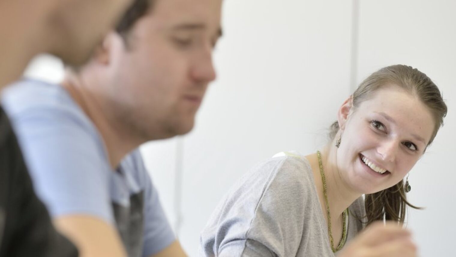 Drei Personen sitzen in einer Reihe, eine Frau schaut lächend zu zwei Männern.