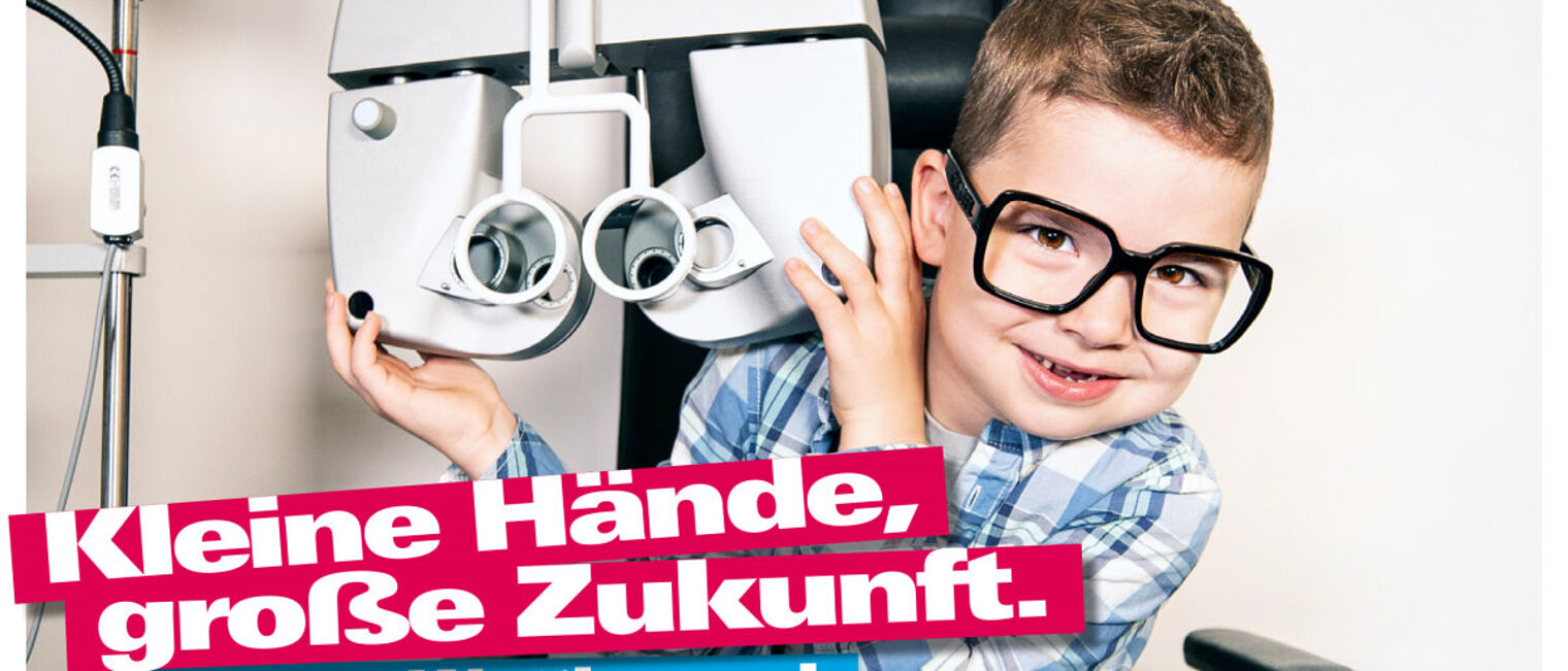 Kleiner Junge mit großer Brille neben einem Sehstärken-Messgerät beim Augenoptiker. Darunter Text Kleine Hände, große Zukunft