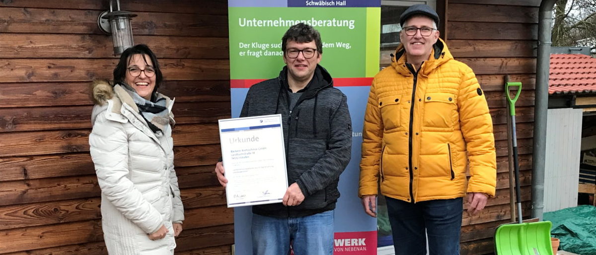 (von links) Christina Bauer, Markus Kretzschmar und Bernd Schöller. Drei Personen stehen nebeneinander und schauen in die Kamera, Mann in der Mitte hält eine gerahmte Urkunde in der Hand.