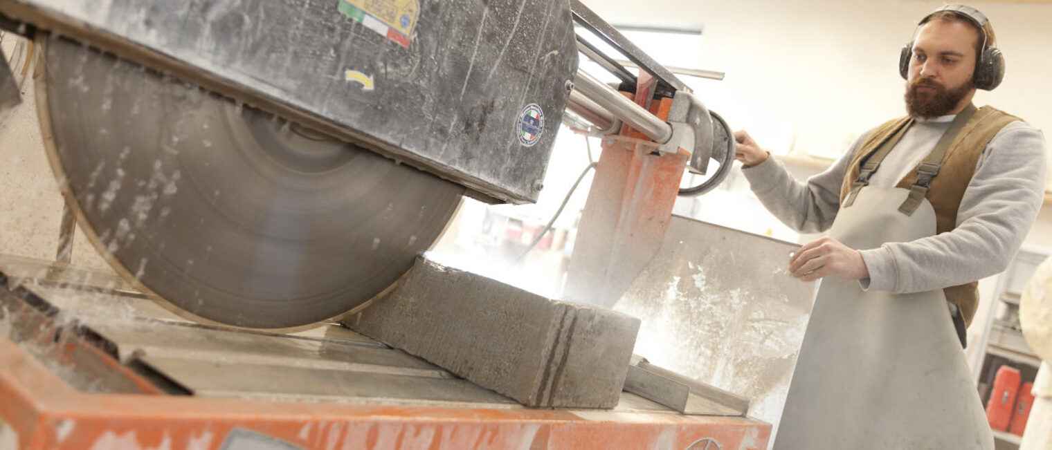 Die Konjunktur im Handwerk entwickelte sich im 4. Quartal 2021 gut. Mann in Arbeitskleidung sägt mit einer großen maschinellen Säge einen Steinblock in einer Werkstatt.