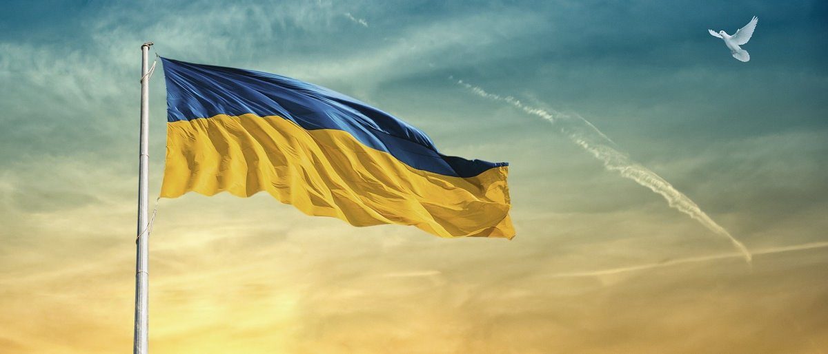 Informationen für Handwerksbetriebe zum Krieg in der Ukraine Eine blau-gelbe Fahne weht von einem Fahnenmast vor einem blau-gelben Himmel mit Wolken, rechts oben eine weiße Taube im Flug