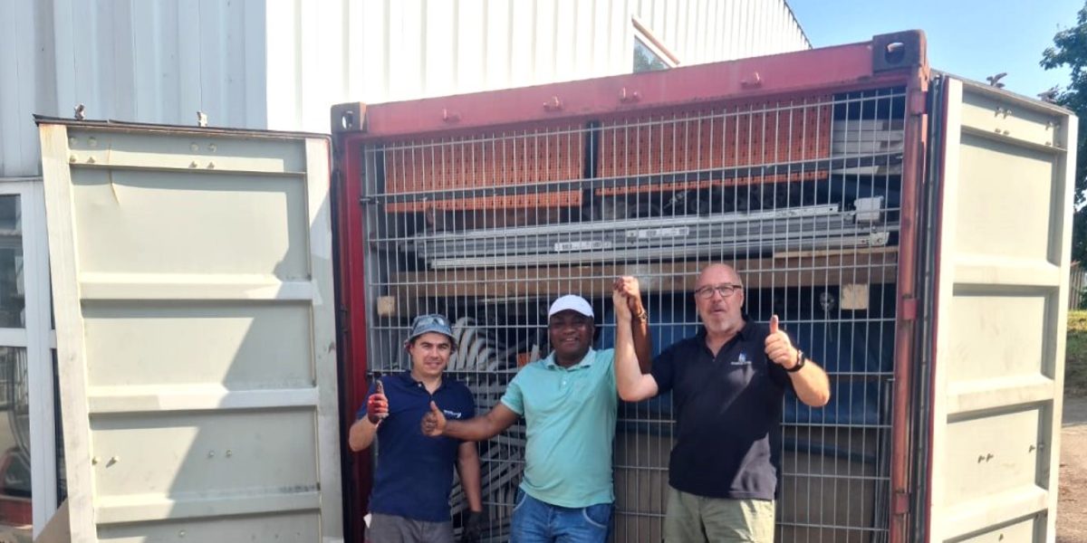 Drei Männer stehen auf einem Betriebsgelände vor einem vollen Schiffscontainer mit offenen Toren und freuen sich.