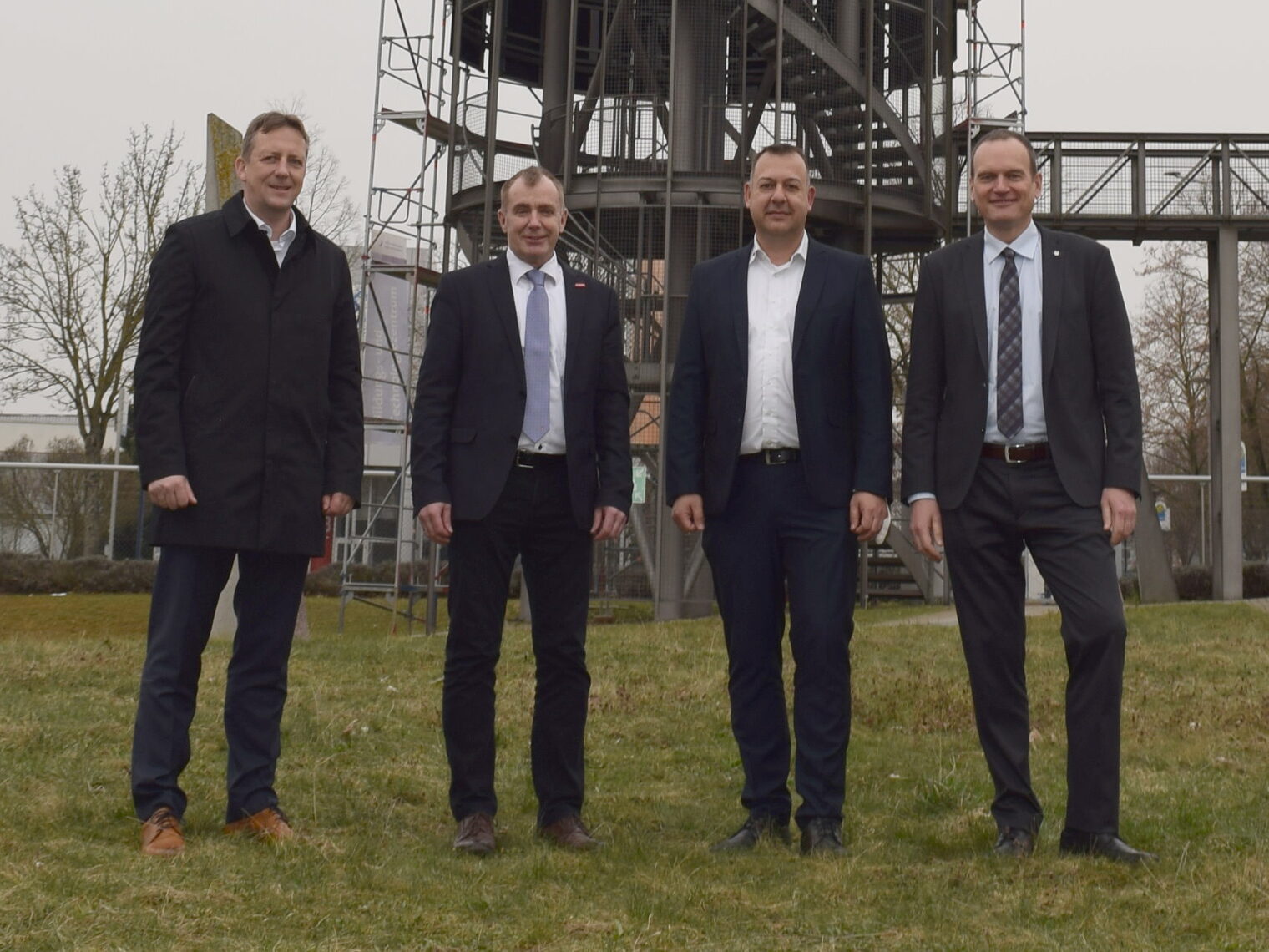 Von links: Ralf Schnörr, Johannes Richter, Timo Bauer und Christoph Blessing. Vier Männer stehen auf einer Grünfläche mit Blick in die Kamera. Im Hintergrund ist ein Stahlturm zu erkennen.