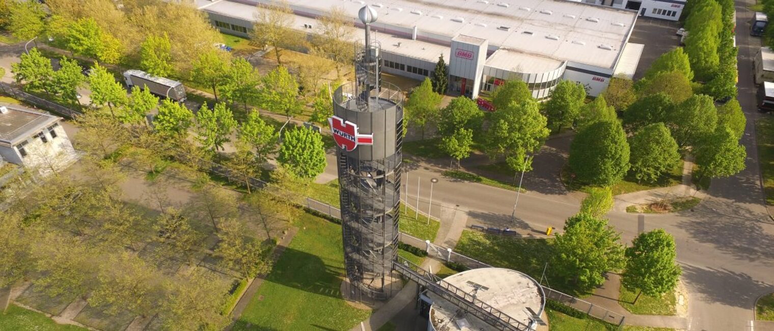 Am Würth-Solarturm wurden die Module ausgetauscht. Drohnenaufnahme des Würth-Solarturms. Im Hintergrund steht ein Firmengebäude.