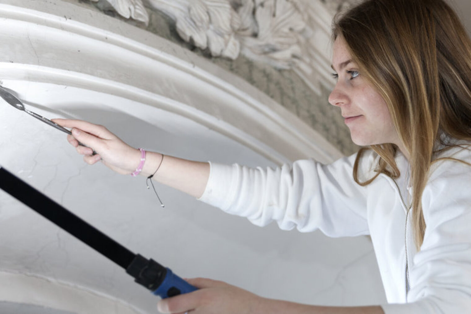 Junge Frau arbeitet mit Werkzeug an einem Riss im Stuck eines Stuckbogens. In der linken Hand hält sie eine Lampe.