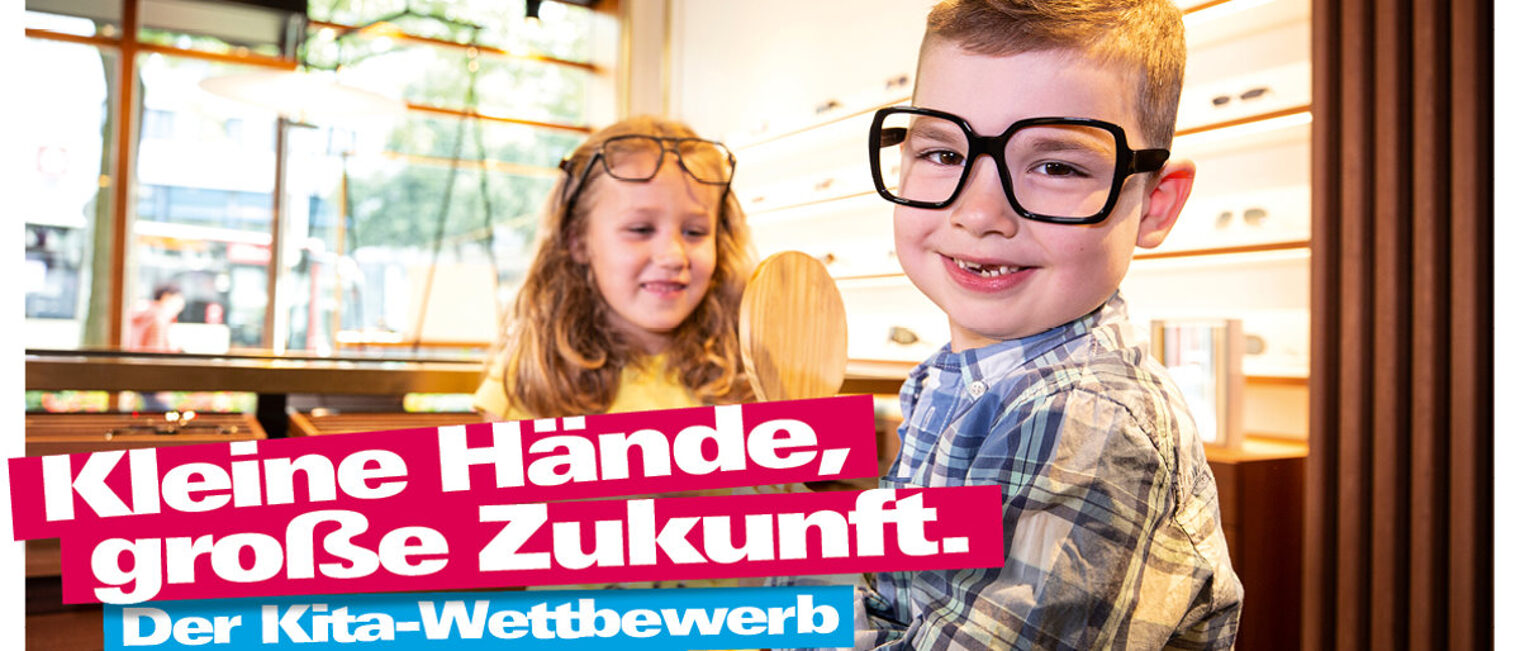 Bis 20. Mai können Betriebe und Kitas noch am Wettbewerb teilnehmen. Zwei Kinder probieren in einem Augenoptiker-Geschäft Brillen, Schriftzug "Kleine Hände, große Zukunft. Der Kita-Wettbewerb"
