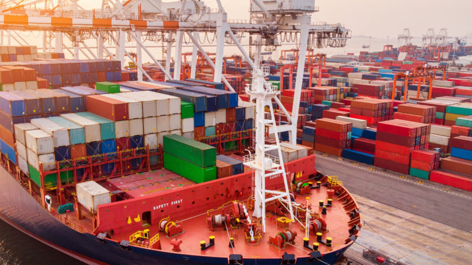 Ein im Hafen liegendes großes Containerschiff wird mit einem Frachtkran beladen.