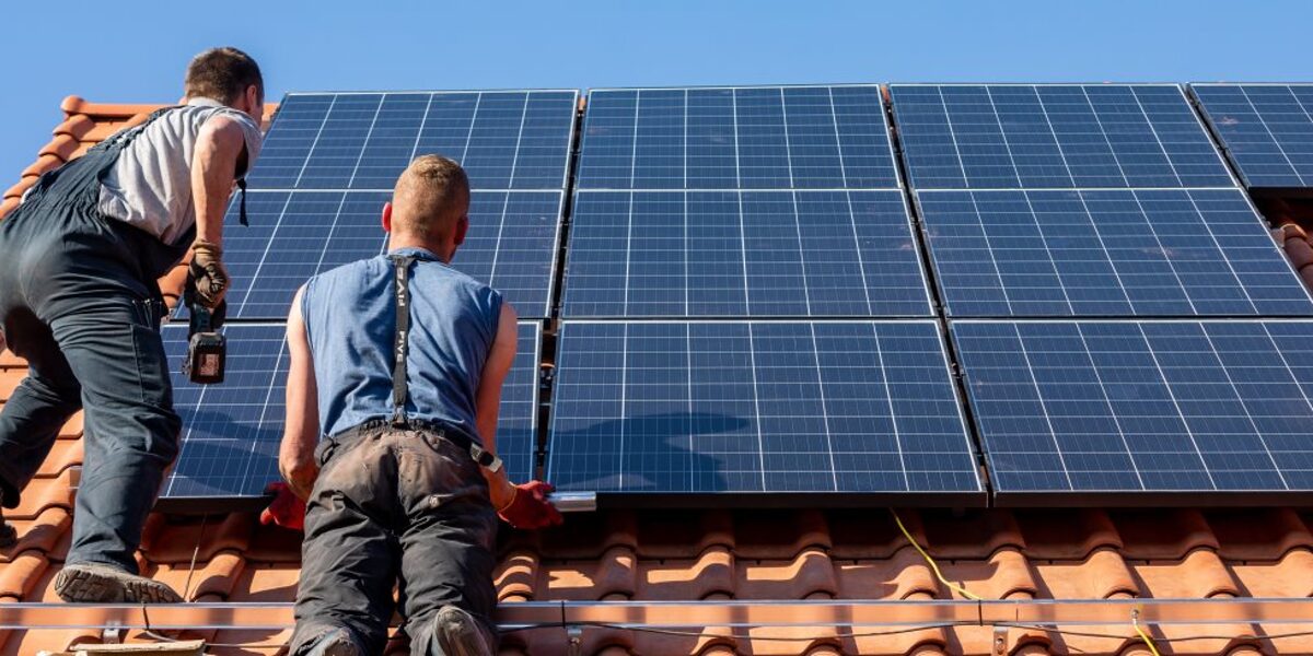 Zwei Männer installieren auf einem Dach eine Photovoltaikanlage.